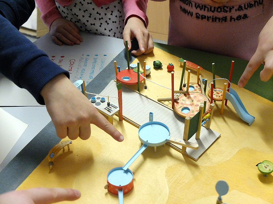 Spielplatzmodell und zeigende Kinderhände