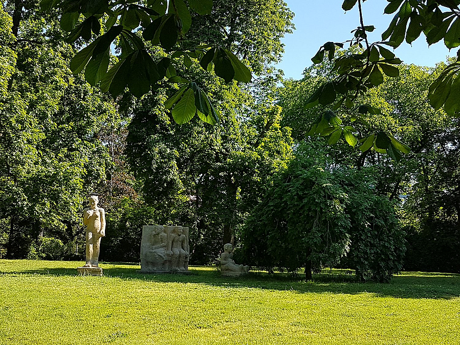 Rasen, im Hintergrund weiße Figurengruppe und Bäume