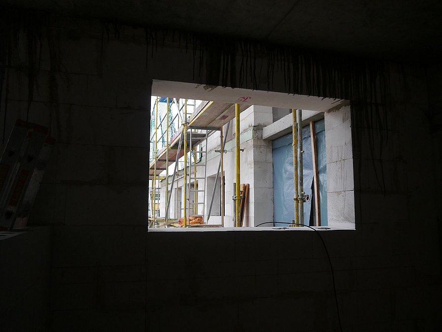 Blick aus dem Dunklen durch Fensteröffnung auf Neubaufassade mit Gerüst