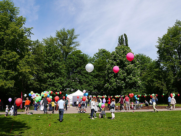 Wiese mit Menschen und Luftballons im Hintergrund