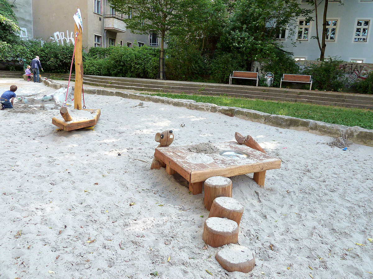Sandfläche mit Spielboot und Backtisch mit hölzerner Maus, Rasen, Stufen, Bänke