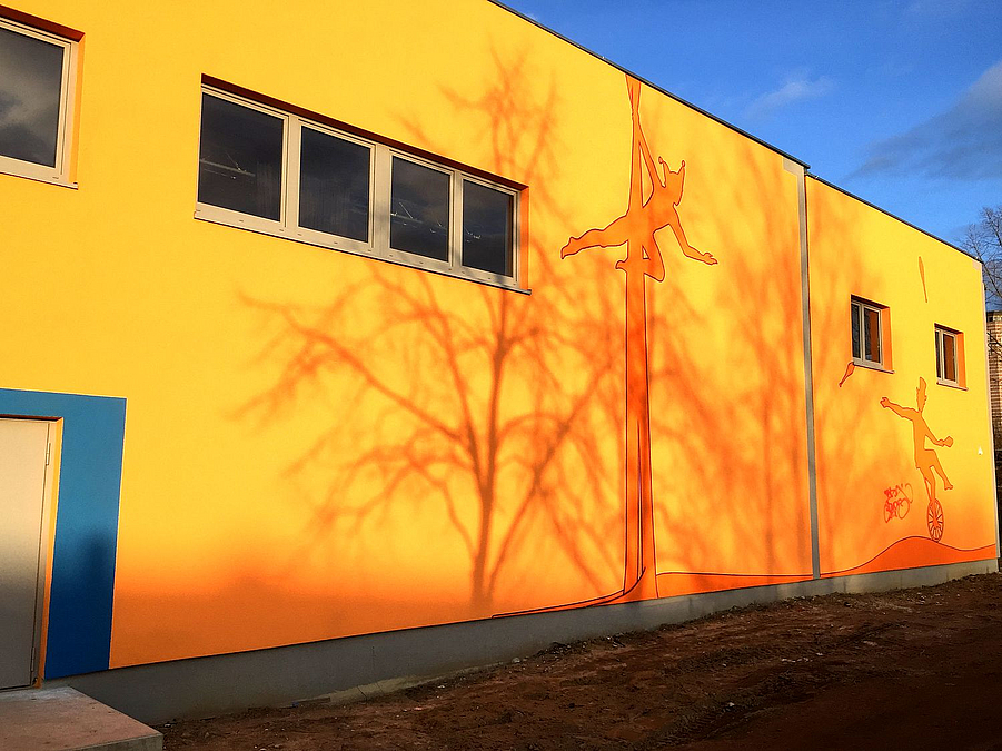 Orangegelbe Fassade mit Fensterreihe und Bild Vertikalseilartistik sowie Jonglage