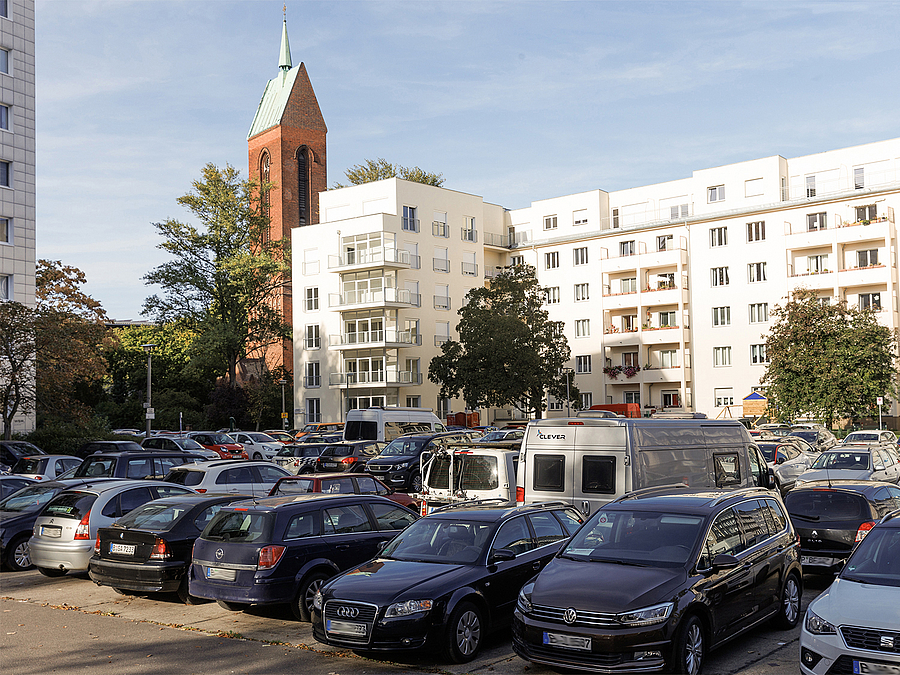 Parkplatz vor moderner Wohnbebauung und Kirche