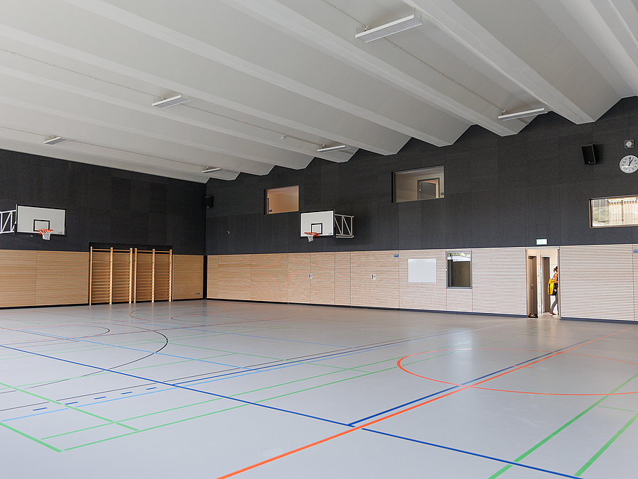 Sporthalleninneres mit heller gefalteter Decke, Holzprallwand und schwarzen Wänden