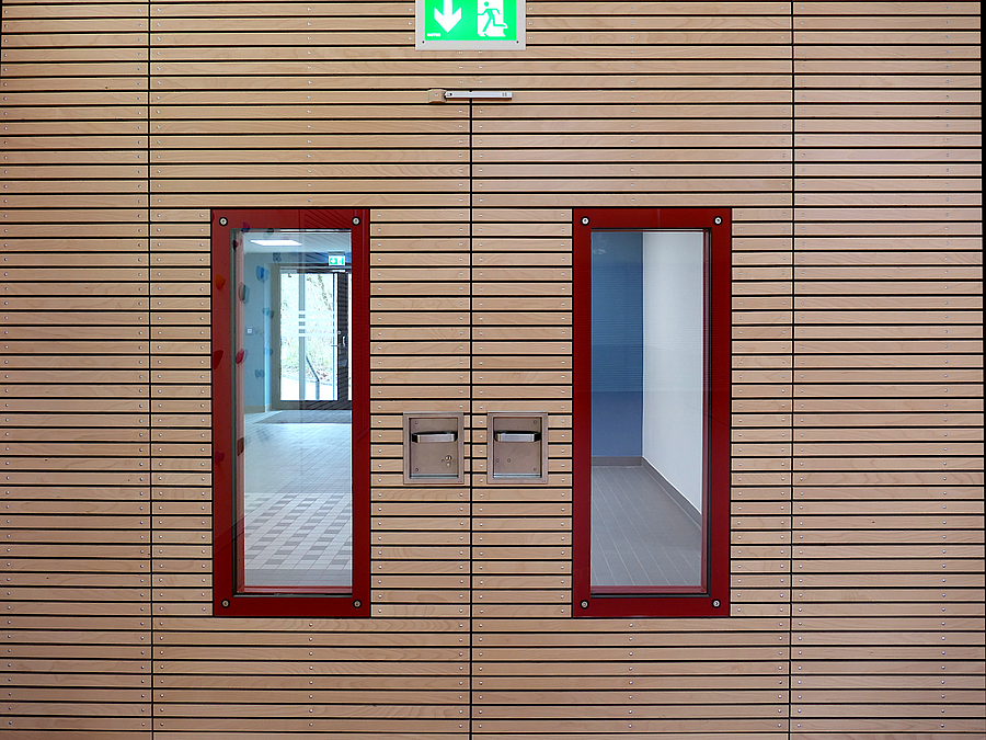 Tür in Holzlamellenwand mit rot gefassten Fenstern