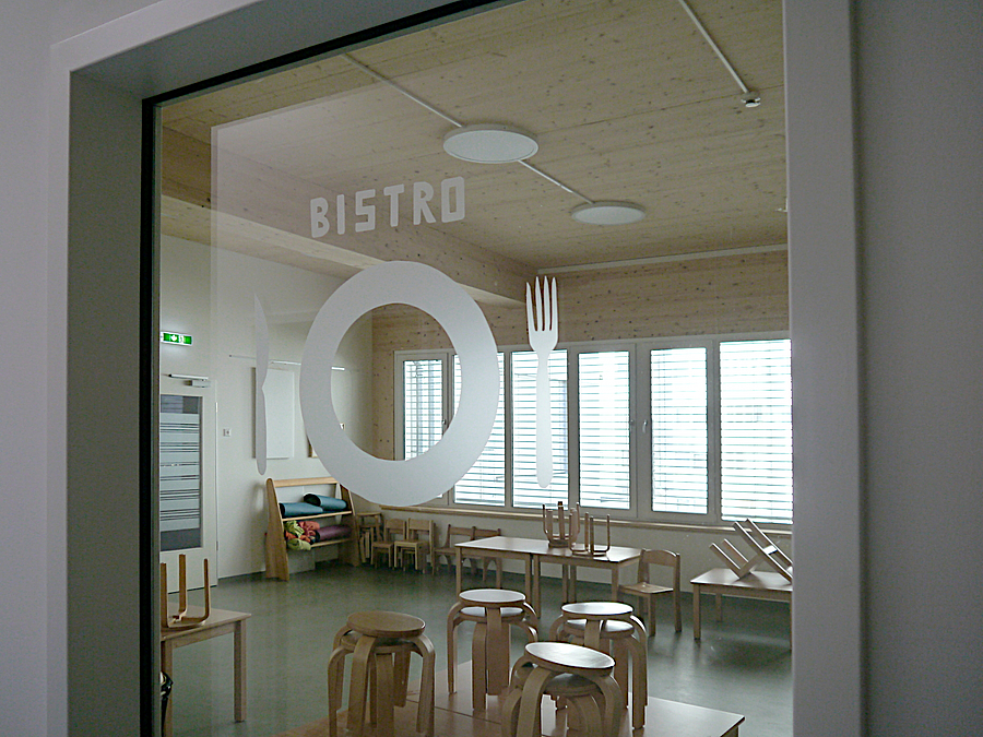 Blick durch Glastür mit Aufschrift "Bistro" auf Speisesaal mit Kindertischen