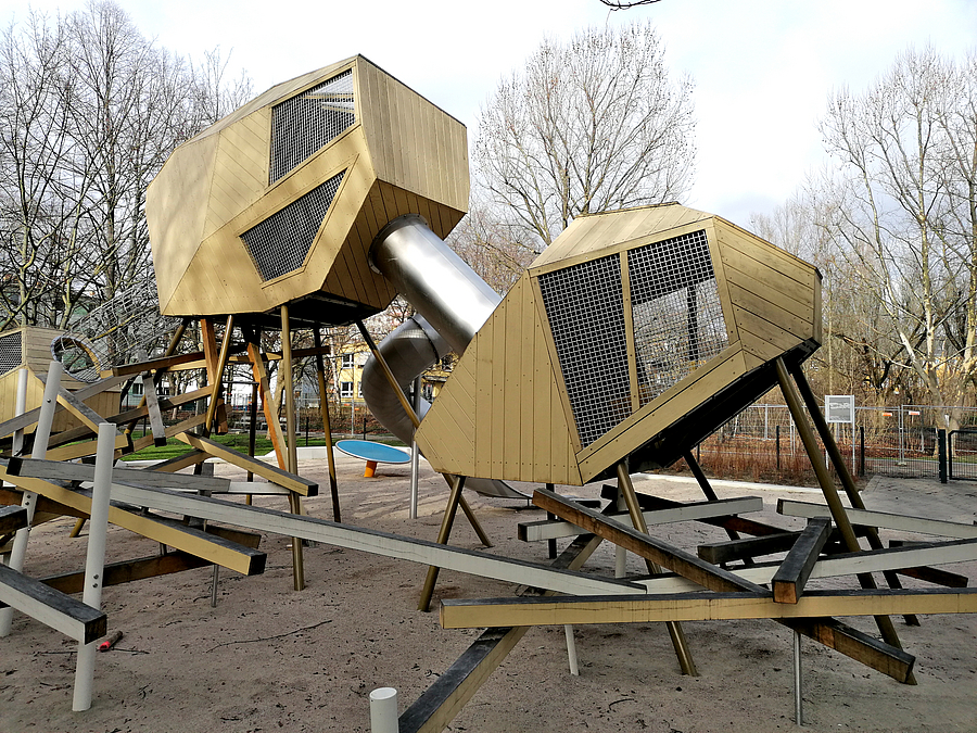 Spielplatz mit Klettergerät mit mehreren geschlossenen Körpern in unterschiedlicher Höhe, Metallröhre und Balancierbalken