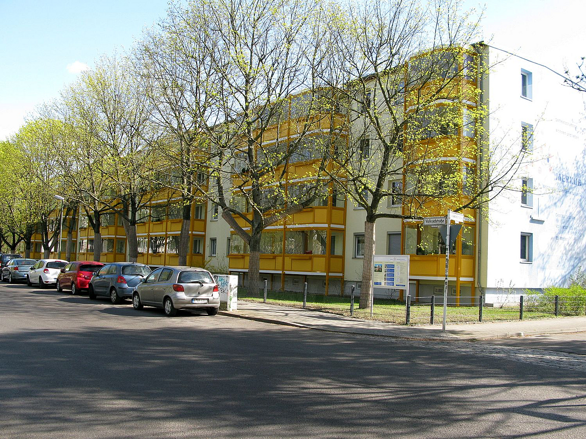 Viergeschosser mit aufgeständerten gelben Balkonen an der Straße mit Bäumen im Frühling