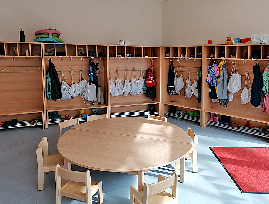 Garderobenregale entlang der Wände, runder Tisch mit Kinderstühlen