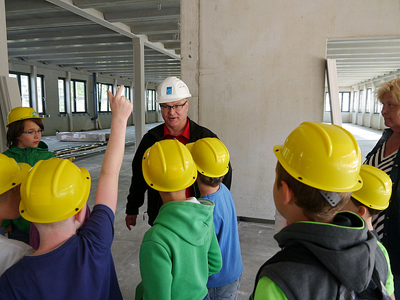 Kinder mit Schutzhelmen auf Baustelle mit Bauleiter