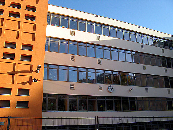Schulfassade mit durchgehenden Fensterbändern, orangefarbenes, vorstehendes Treppenhaus mit kleinen Fenstern