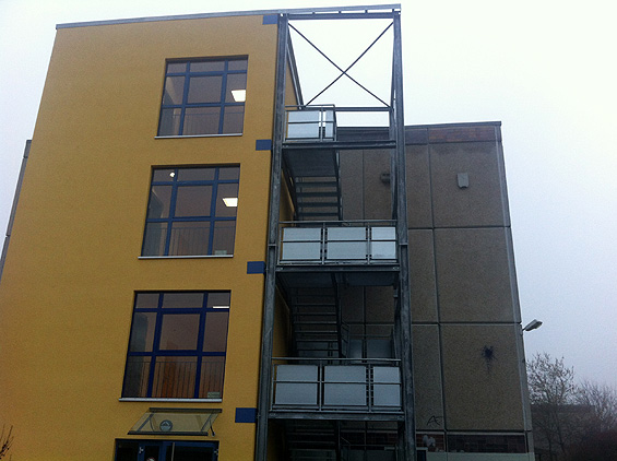 Gelber Anbau mit Fenstern, daneben Außentreppe aus Stahl mit Plattformen